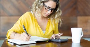 Woman calculating the total cost of a debt settlement plan with a calculator and notebook