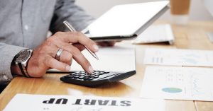 Person calculating business startup costs with a calculator and financial charts