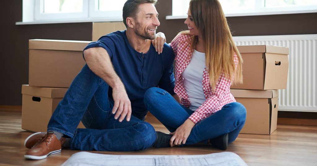 Couple sitting beside moving boxes with a house plan spread on the floor
