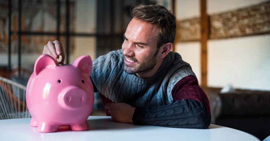 Man putting a coin into a pink piggy bank at home