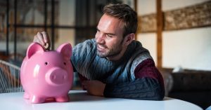 Man putting a coin into a pink piggy bank at home