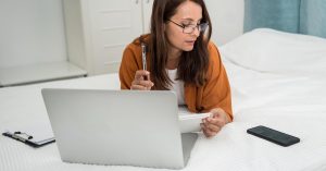 Woman reviewing notes while checking financial information on a laptop