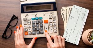 Hands using a calculator beside a paycheck and cash