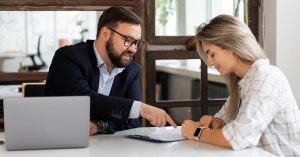 Woman signing a document while another person points to the paperwork