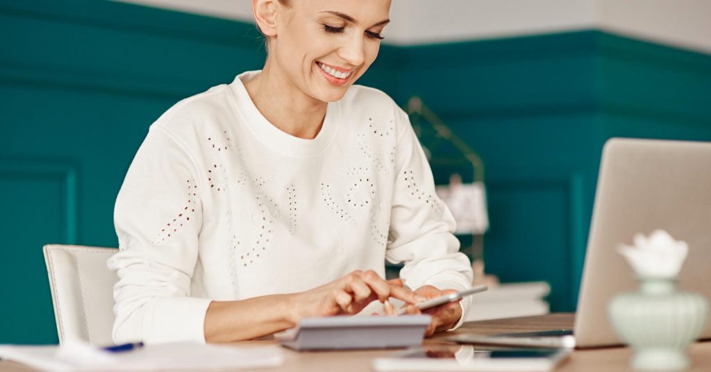 Woman using a smartphone beside an open laptop
