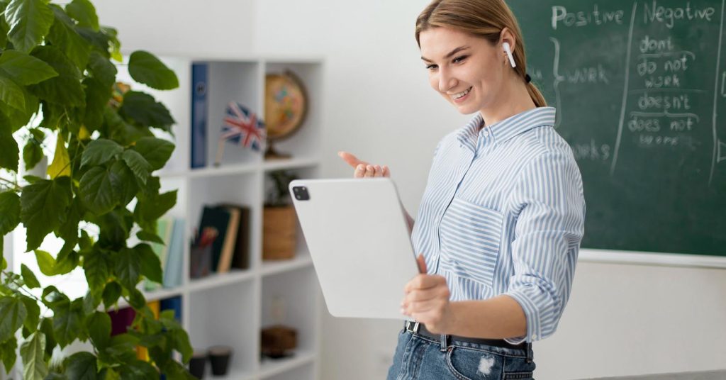 Woman holding a tablet in front of a chalkboard with English grammar notes