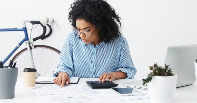 Woman reviewing household expenses with a calculator and financial documents