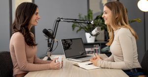 Two women talking into microphones across a table with a laptop