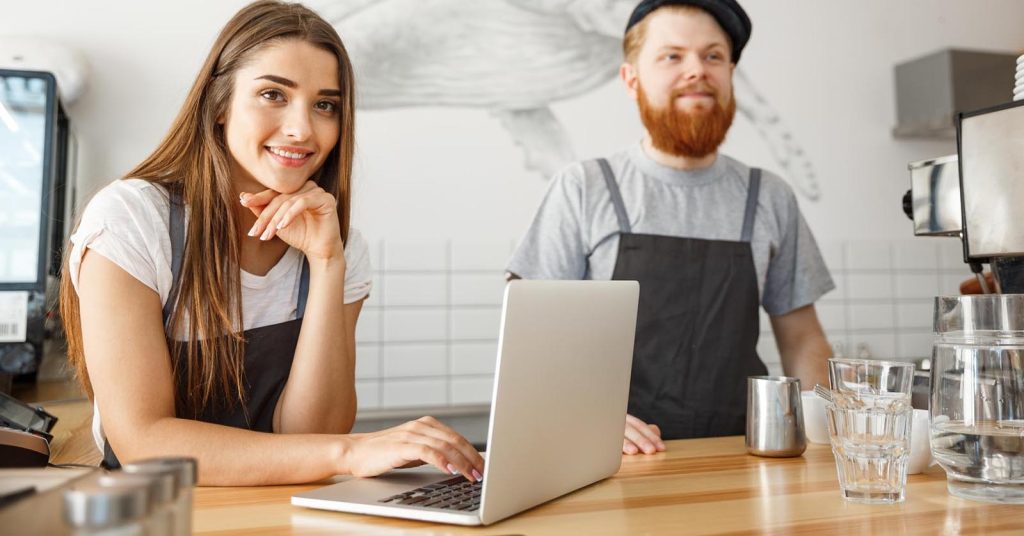 Two cafe owners standing behind the counter with a laptop