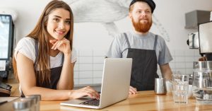 Two cafe owners standing behind the counter with a laptop