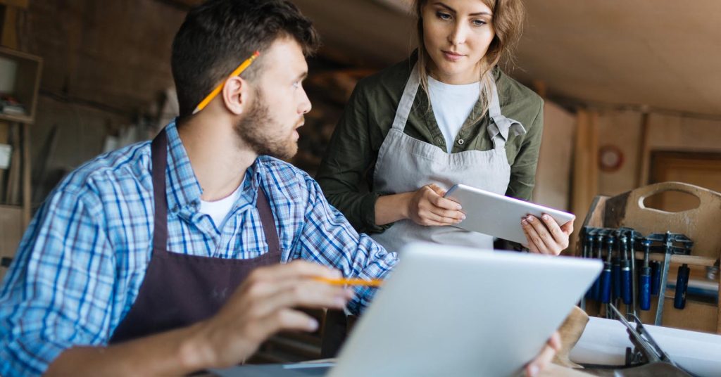 Small business owners reviewing plans on a laptop and tablet in their workshop