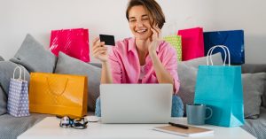 Woman holding a credit card while shopping online with shopping bags around her