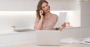Woman speaking on the phone while holding a document beside a laptop