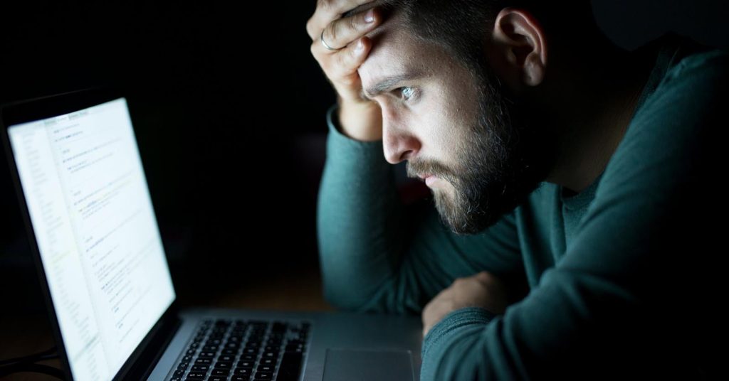 Concerned man looking at a laptop screen in a dark room