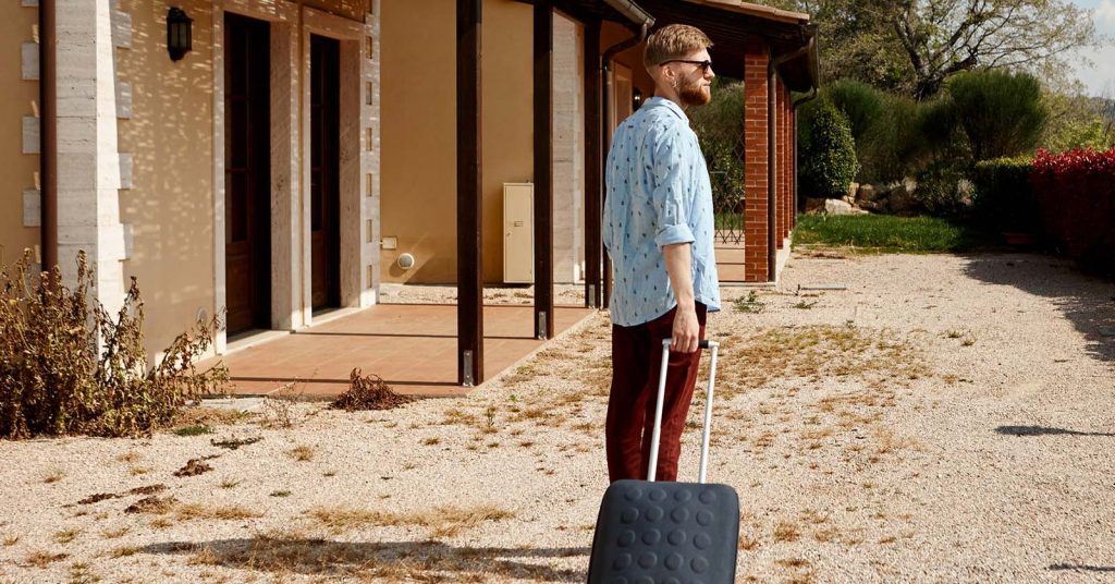 Man standing outside a house with a rolling suitcase