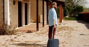 Man standing outside a house with a rolling suitcase