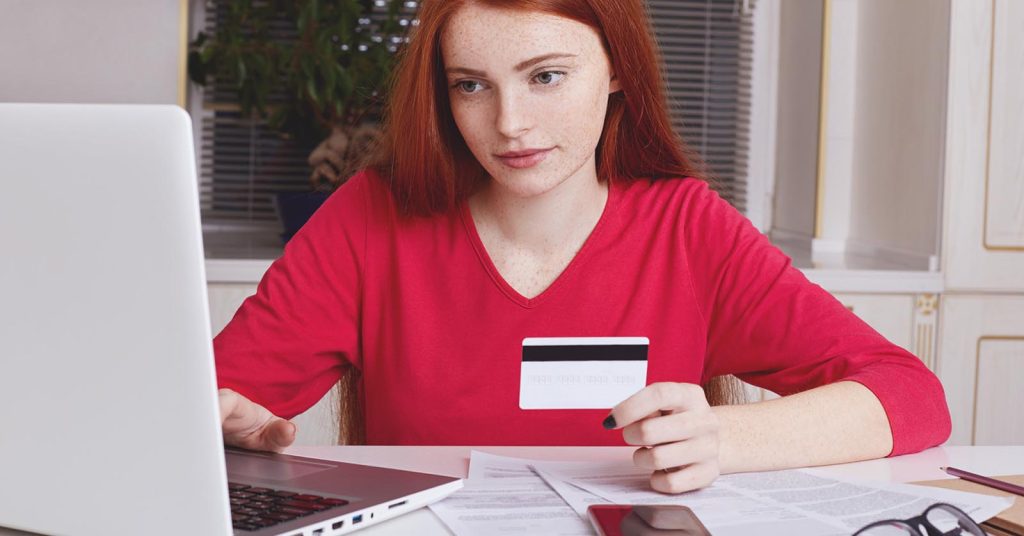 Woman holding a credit card while reviewing an application on a laptop