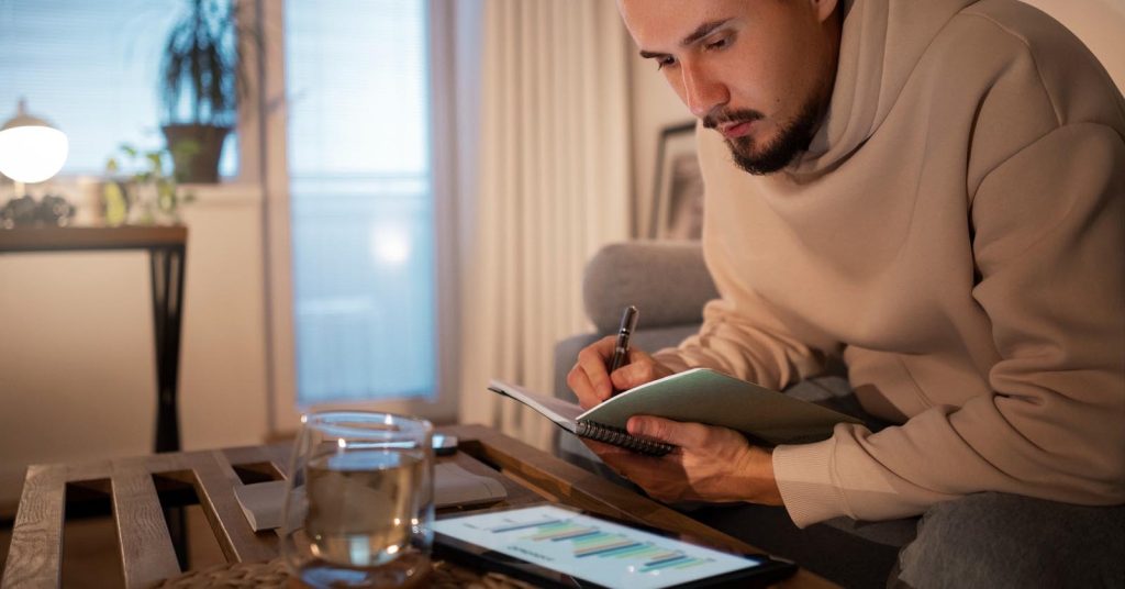 Freelancer reviewing uneven monthly income on a tablet while planning debt payments in a notebook