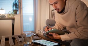 Freelancer reviewing uneven monthly income on a tablet while planning debt payments in a notebook