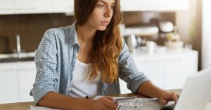 Woman reviewing financial documents and a laptop at home