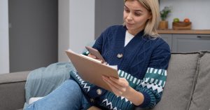 Woman reviewing notes on a clipboard while sitting on a sofa at home