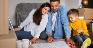 Two adults and a child looking at a house plan beside moving boxes