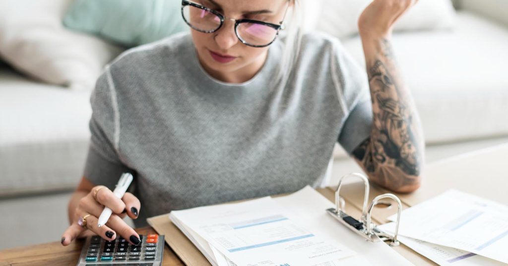 Woman reviewing bills and expenses with a calculator at home