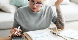 Woman reviewing bills and expenses with a calculator at home