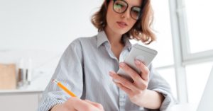 Woman comparing savings, investment, and debt payoff options on her phone and notebook