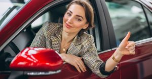 Woman sitting in a red car and giving a thumbs-up
