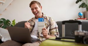 Man holding a passport and boarding passes while planning a trip on a laptop