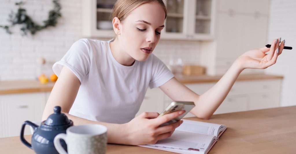 Woman looking at a smartphone while sitting at a table with an open notebook