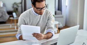 Man reviewing financial documents beside a laptop