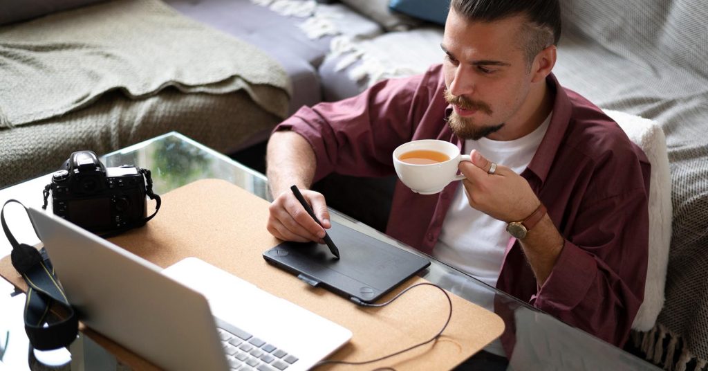 Person working on a creative side hustle from home using a laptop and drawing tablet