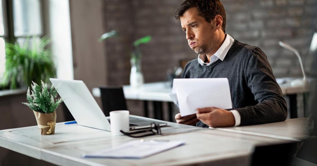 Small business owner reviewing financial paperwork beside a laptop