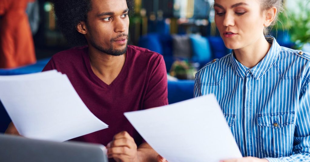 Two people reviewing financial records beside a laptop