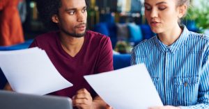 Two people reviewing financial records beside a laptop