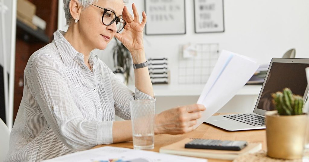 Older woman reviewing financial documents beside a laptop and calculator