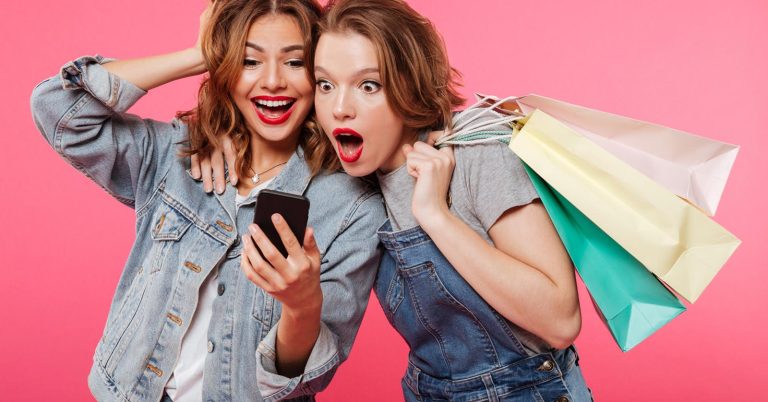 Two women reacting to a shopping deal while holding shopping bags and a smartphone