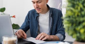 Man reviewing financial paperwork beside a laptop