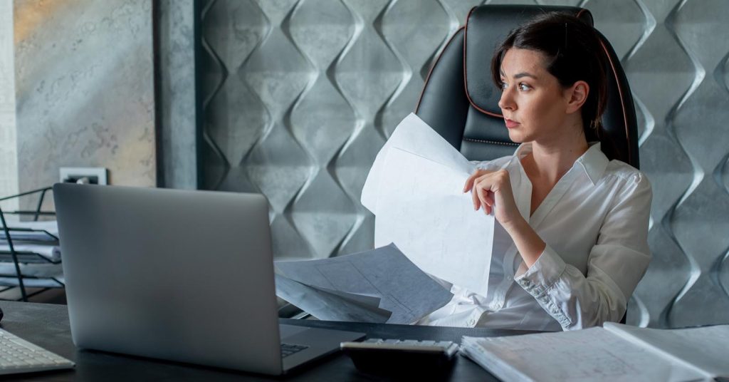 Woman reviewing financial documents beside a laptop