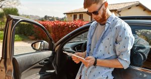 Man using a tablet beside a parked car with the driver door open