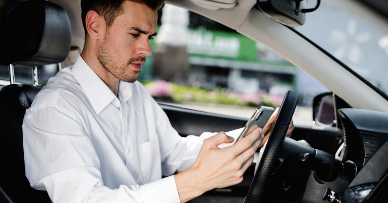 Man checking his smartphone while sitting in a parked car