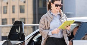 Woman using a tablet while standing beside a parked car