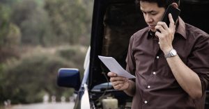 Man speaking on the phone and holding a document beside a car with the hood open