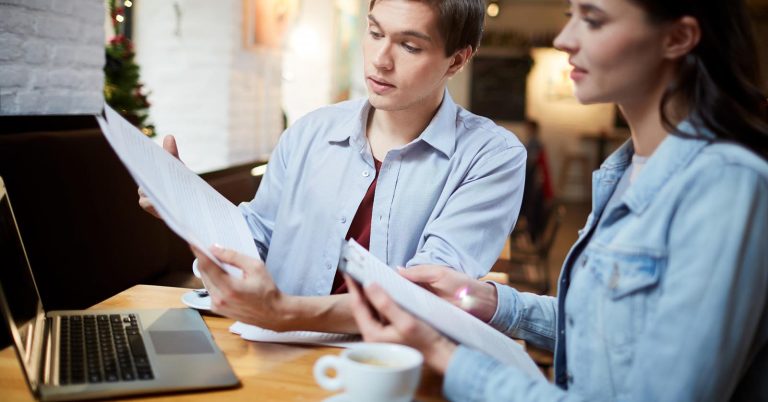 Couple comparing printed documents beside a laptop