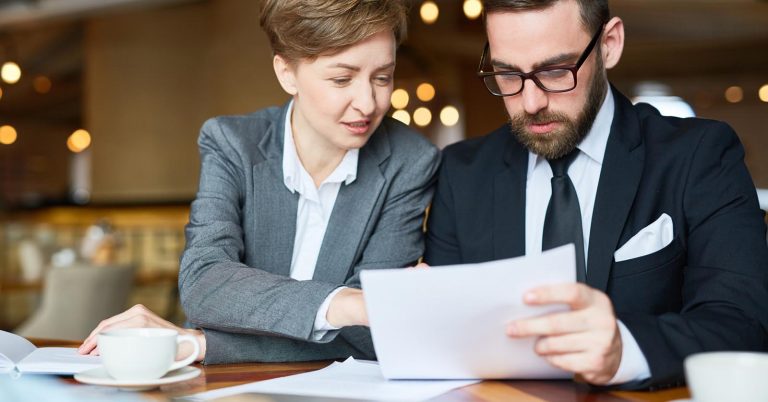 Two professionals comparing documents at a table
