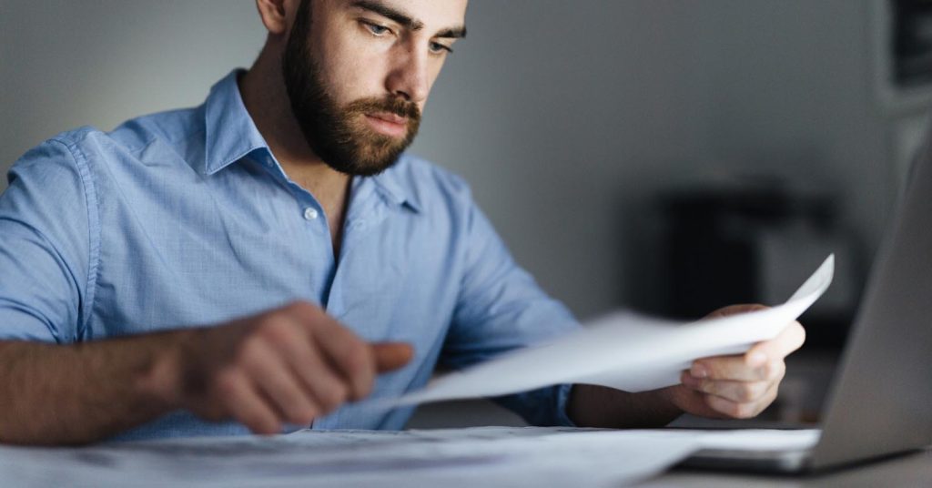 Man reviewing documents beside a laptop