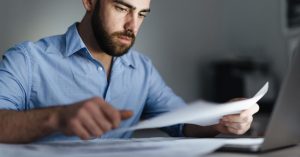 Man reviewing documents beside a laptop