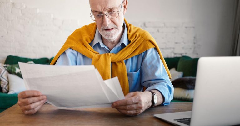 Older man reviewing life insurance claim documents beside a laptop